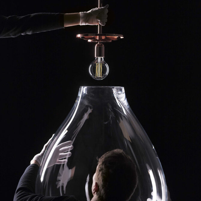 A statement suspension light with a generous blown glass shade and exposed filament bulb. The warm copper detail contrasts beautifully with the clear glass, highlighting its sculptural form and refined craftsmanship.